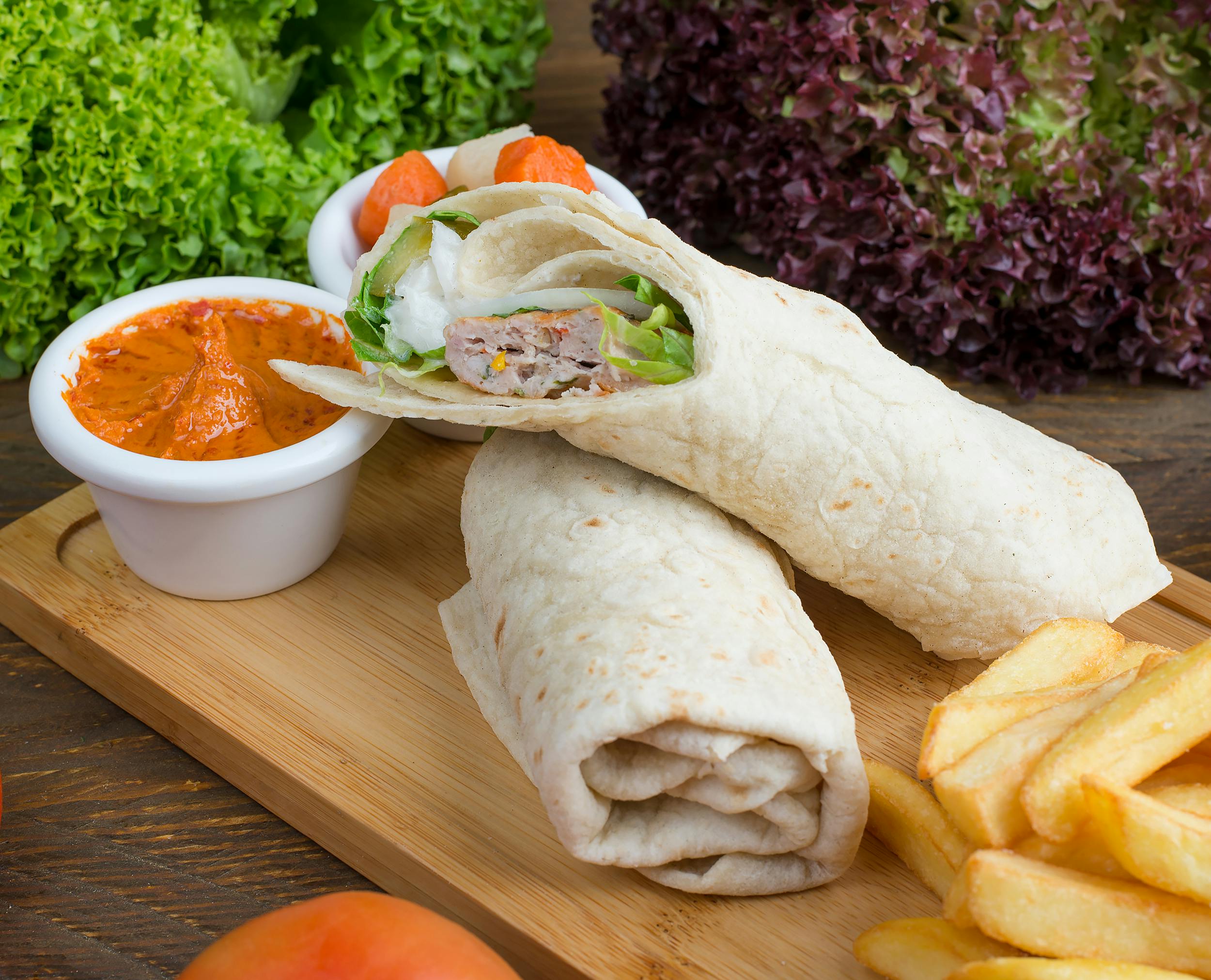 Tasty wraps served with fries and a spicy dip on a wooden platter.