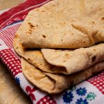 Close-up of homemade roti stacked on a traditional colorful cloth, freshly made.